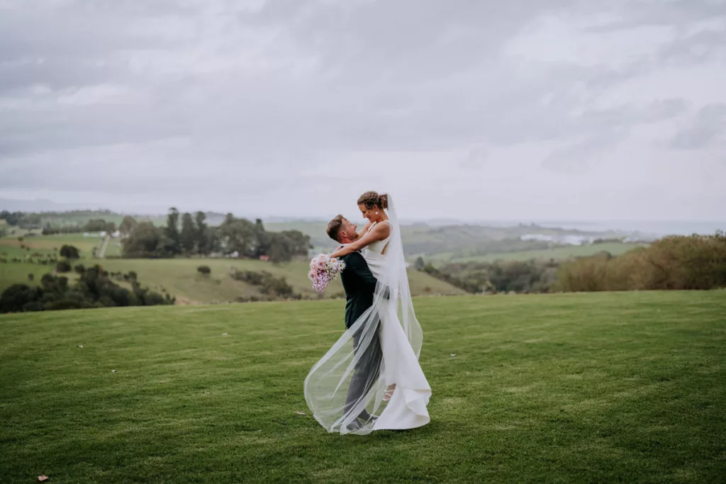 Bride and groom walking through the grounds of Greyleigh Kiama with rolling hills in the background