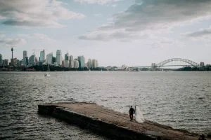 Bradleys Head wedding photo of bride and groom walking on jetty with Sydney Harbour Bridge and Opera House in the background