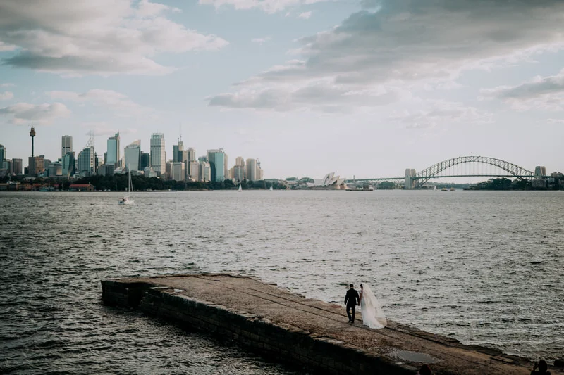 Bradleys Head wedding photo of bride and groom walking on jetty with Sydney Harbour Bridge and Opera House in the background