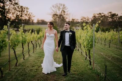 Bride and groom holding hands at sunset outside Enzo Hunter Valley with vineyards in the background