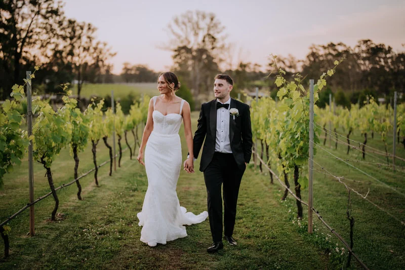 Bride and groom holding hands at sunset outside Enzo Hunter Valley with vineyards in the background